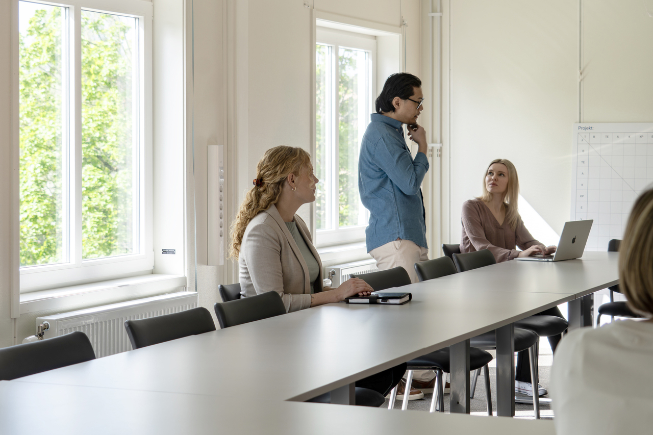 Möte i konferensrum i kontorsmoduler från Expandia i Skanskas projektkontor i Karlstad. Flera personer sitter runt ett långt bord i samtal och arbete, med datorer och anteckningar framme. Rummet är ljust med stora fönster som släpper in dagsljus.