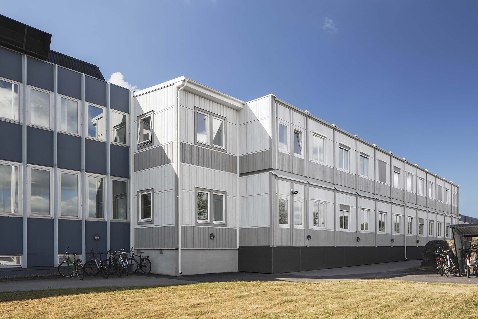 Tvåvånings modulhus från Expandia med kontorslokaler i ljusa grå nyanser, med fönsterrader längs fasaden och cyklar parkerade intill byggnaden.