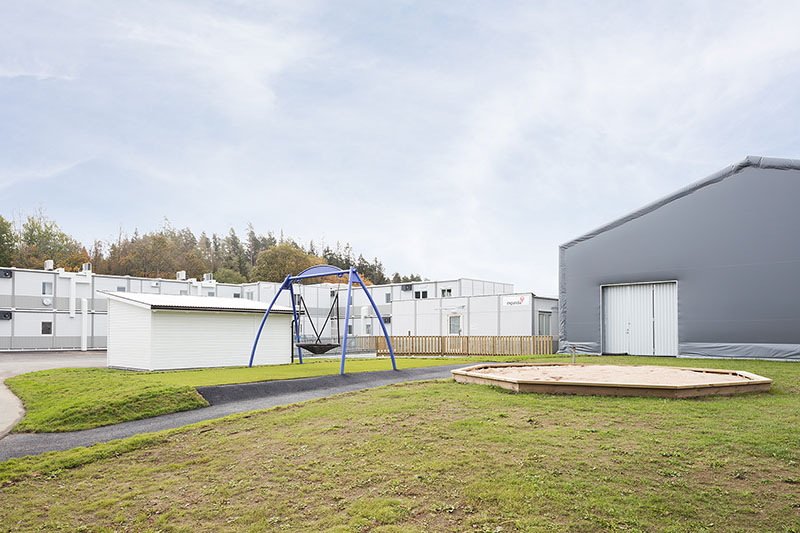 Skolgård vid Kronängsskolan i Borås med lekytor, sandlåda och gungställning, intill en tillfällig idrottshall och en modullösning från Expandia för skolans verksamhet.