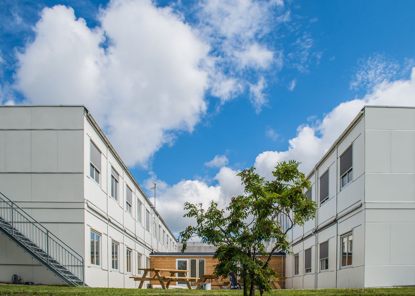 Vita kontorsmoduler i två plan placerade i grön utemiljö med träd och gräsytor. Flexibla kontorsmoduler från Expandia.