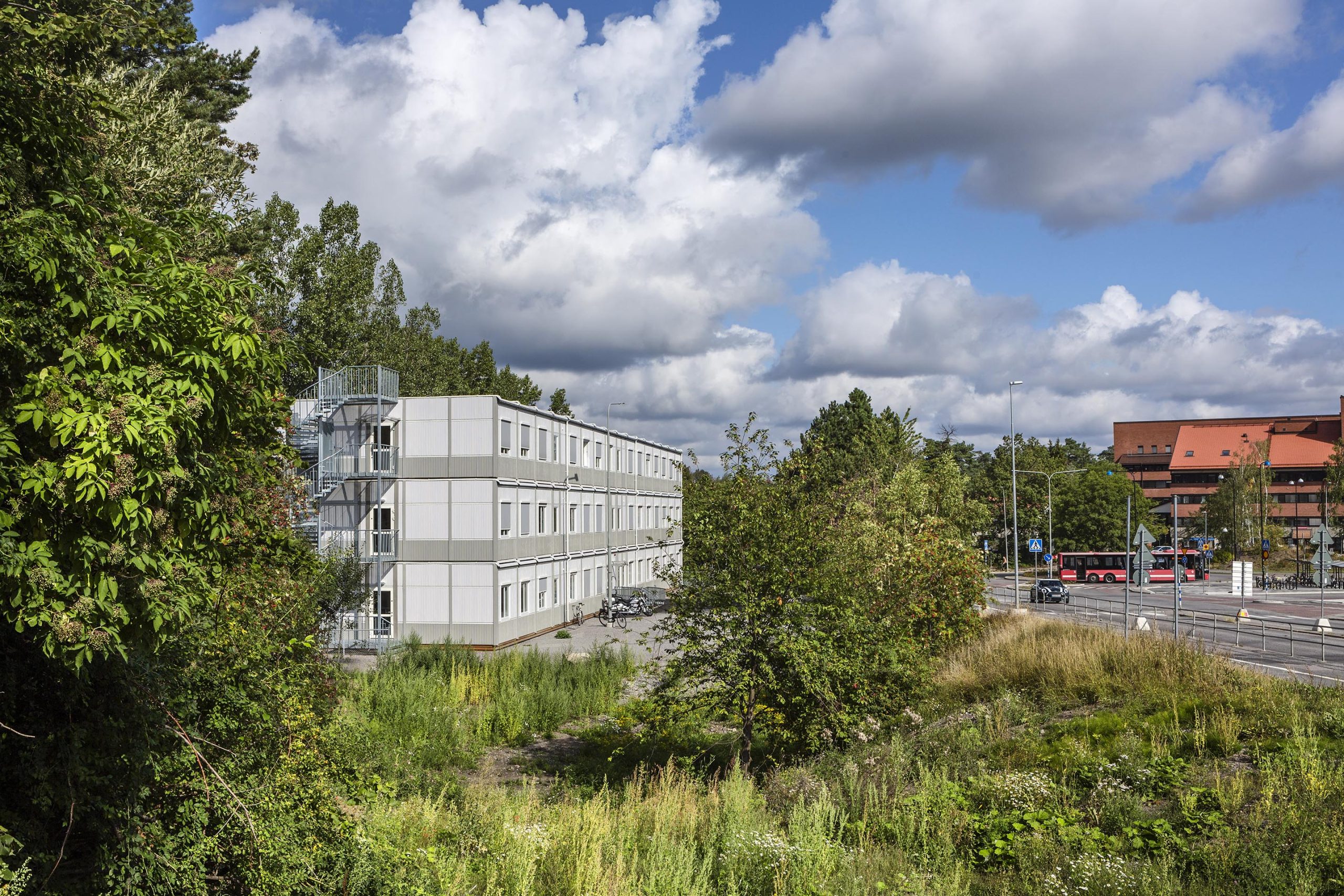 Tillfällig modulbyggnad från Expandia i tre våningar med kontorslokaler, placerad i grön stadsmiljö, med ljus fasad, många fönster och externa trappor.