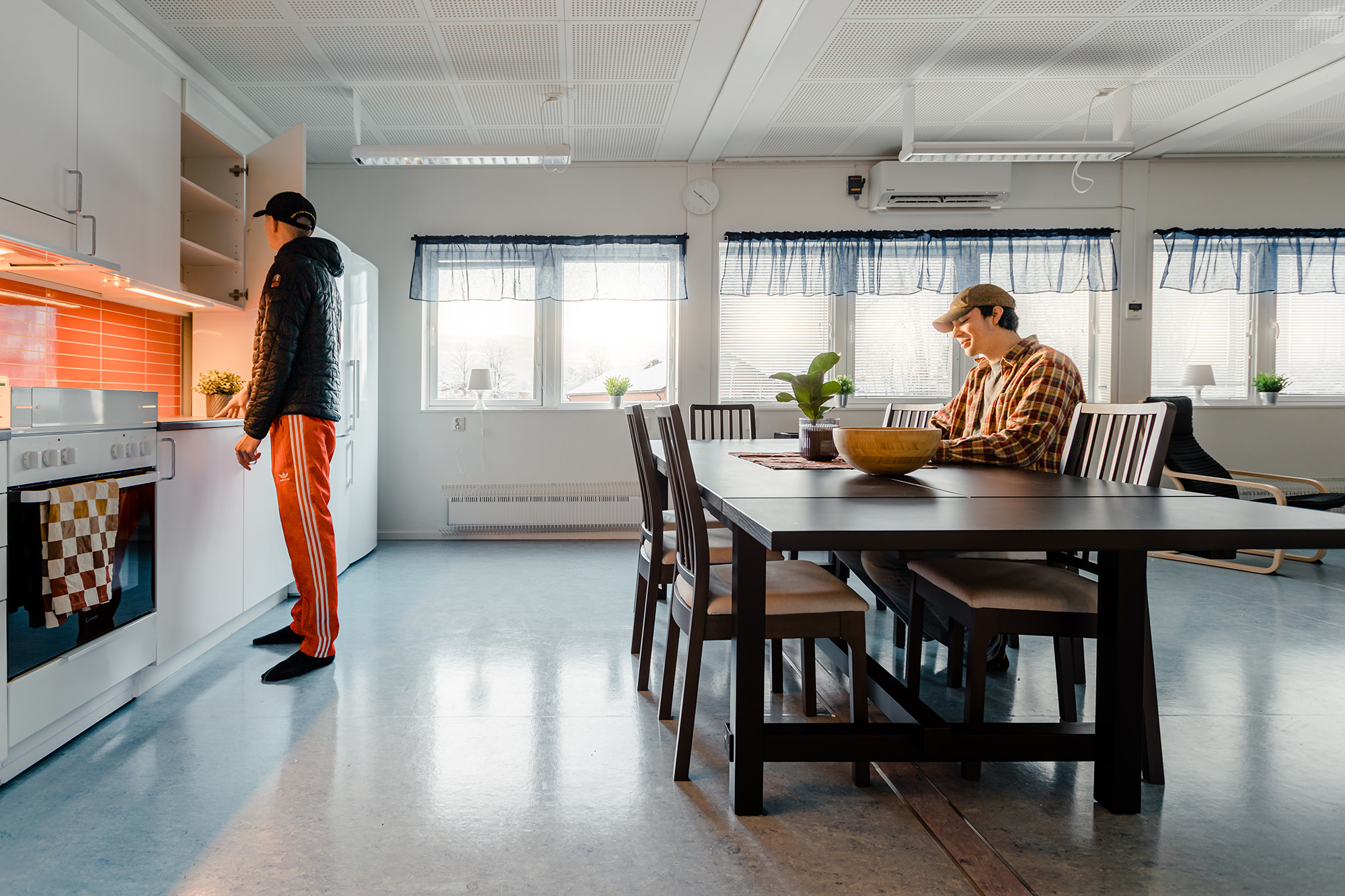 Gemensamt kök och matplats i elevboendemoduler, där två personer förbereder mat och sitter vid matbordet i en ljus och hemtrevlig miljö.