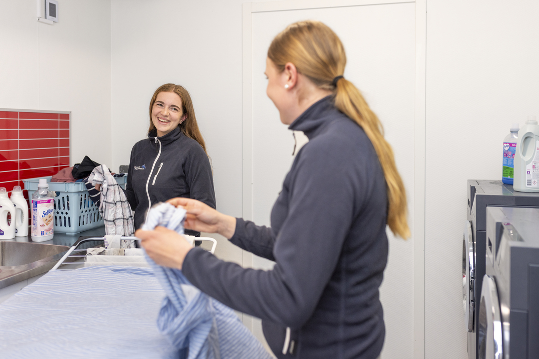 Elever vid Sveriges Ridgymnasium i Svedala är tillsammans i ett tvättrum och viker tvätt. Miljön är ljus och funktionell med tvättmaskiner och arbetsytor.