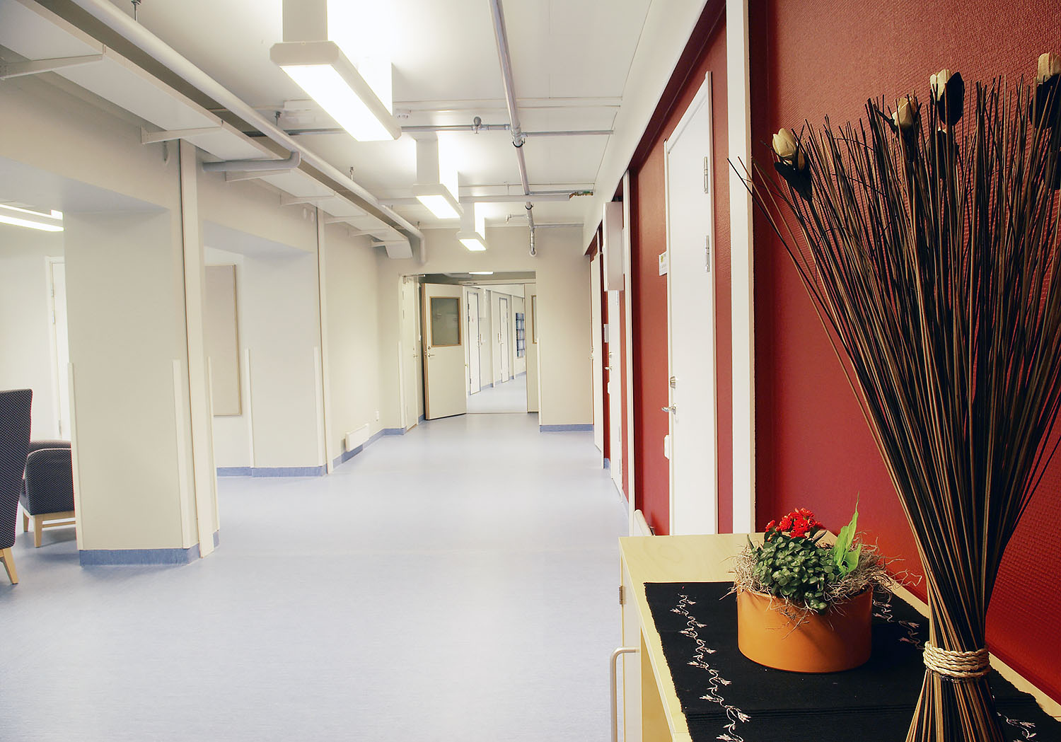 Ljus korridor i äldreboendemoduler från Expandia med röda accentväggar, vita dörrar, jämnt golv och inredningsdetaljer som skapar en trivsam och tillgänglig miljö.