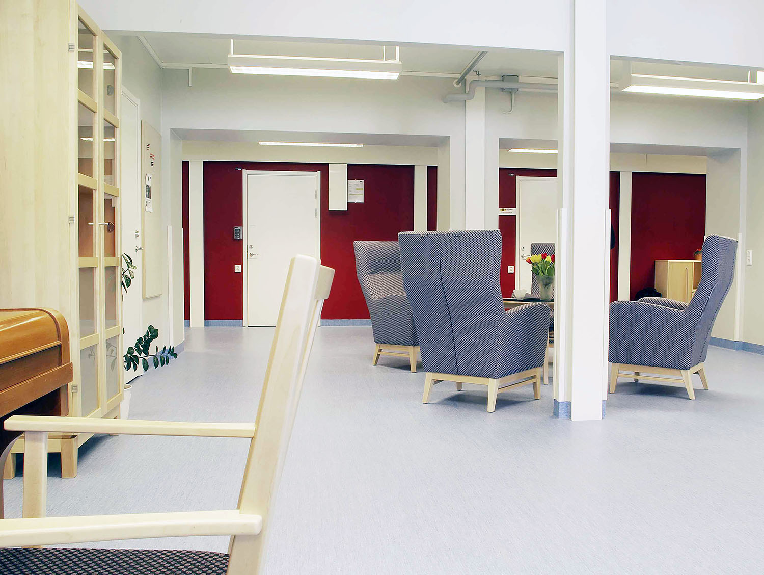 Ljust gemensamhetsutrymme i Vidingehem Bo i Växjö boendemoduler från Expandia med fåtöljer, bord och röda fondväggar anpassat för social samvaro.