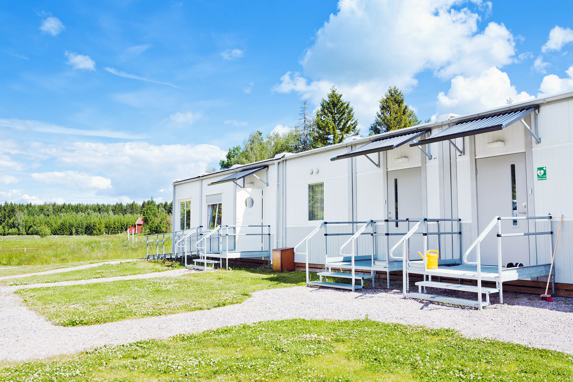 Säfstahill i Vingåker boendemoduler från Expandia, placerade i grön landsbygdsmiljö med entréer, ramper och vit fasad under blå himmel.